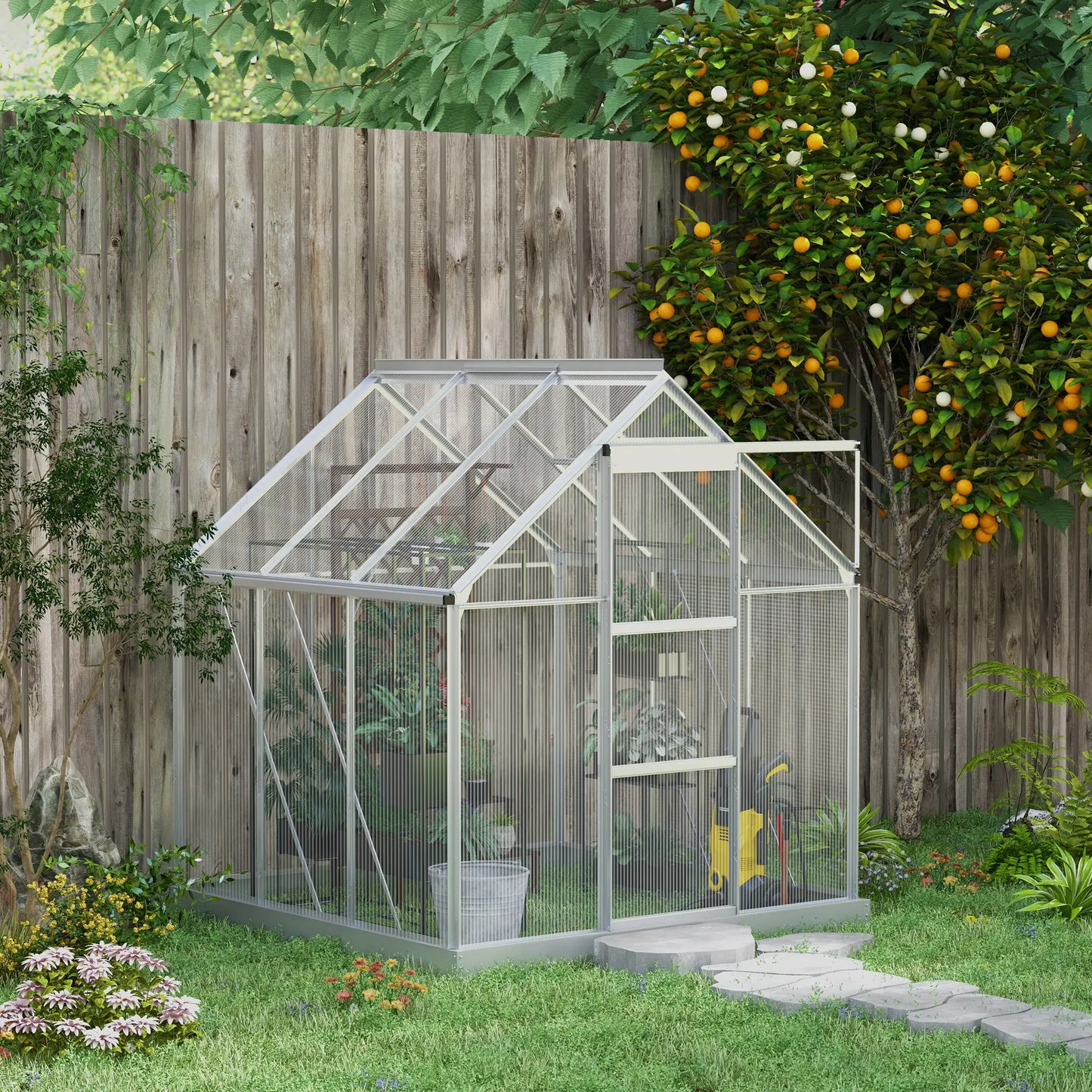 Clear glass greenhouse in a garden with a wooden fence and fruit tree in the background