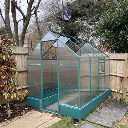 Greenhouse in a garden setting with trees and a fence in the background